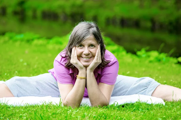 Femme dans sa cinquantaine faire du yoga dans un parc — Photo