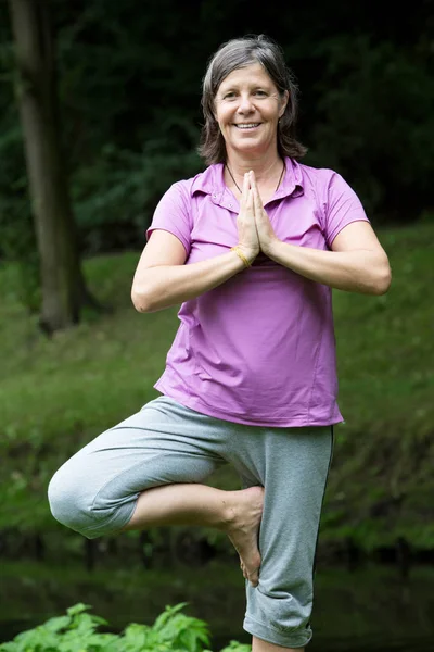 Femme dans sa cinquantaine faire du yoga dans un parc — Photo