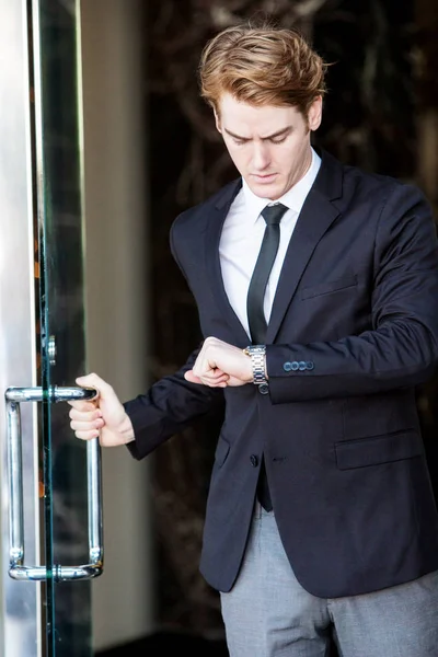 Empresário em uma entrada olhando para seu relógio de pulso — Fotografia de Stock