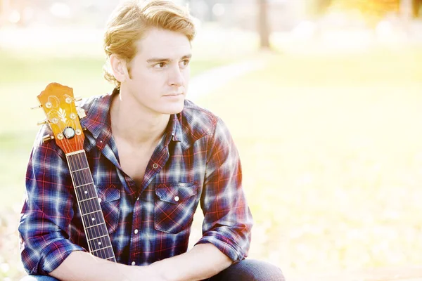 Knappe man zit in het park met gitaar — Stockfoto