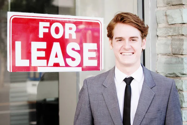Handsome man in suit standing in front of sign For Lease — Stock Photo, Image