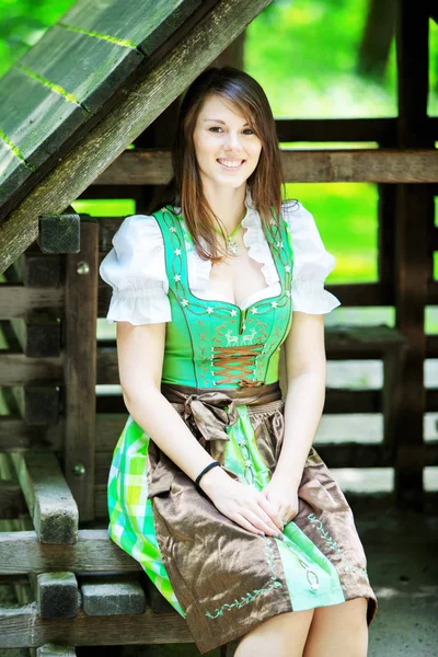 Jovem mulher vestindo um dirndl sentado no alojamento de madeira — Fotografia de Stock