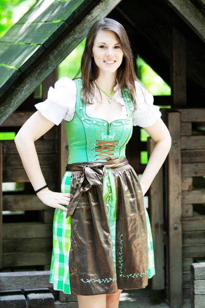 Young woman wearing a dirndl standing at wooden lodge — Stock Photo, Image