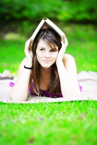 Young woman lying on blanket in park with book on her head — Stock Photo, Image