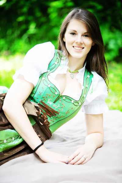 young woman in dirndl lying on blanket in park