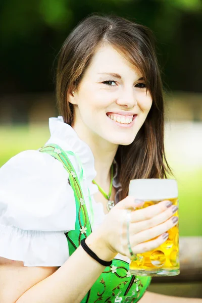 Frau im Dirndl sitzt mit Bier am Tisch im Biergarten — Stockfoto