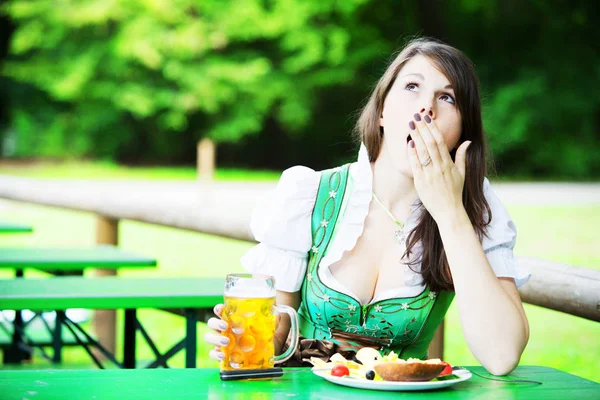 Mulher em dirndl sentado no jardim da cerveja e olhando cansado — Fotografia de Stock
