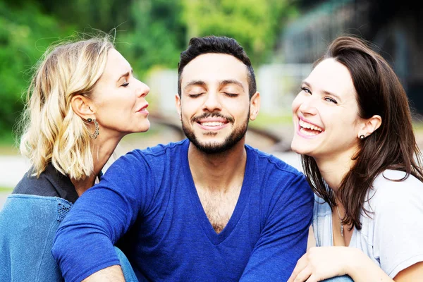 two women kissing handsome man on his cheeks