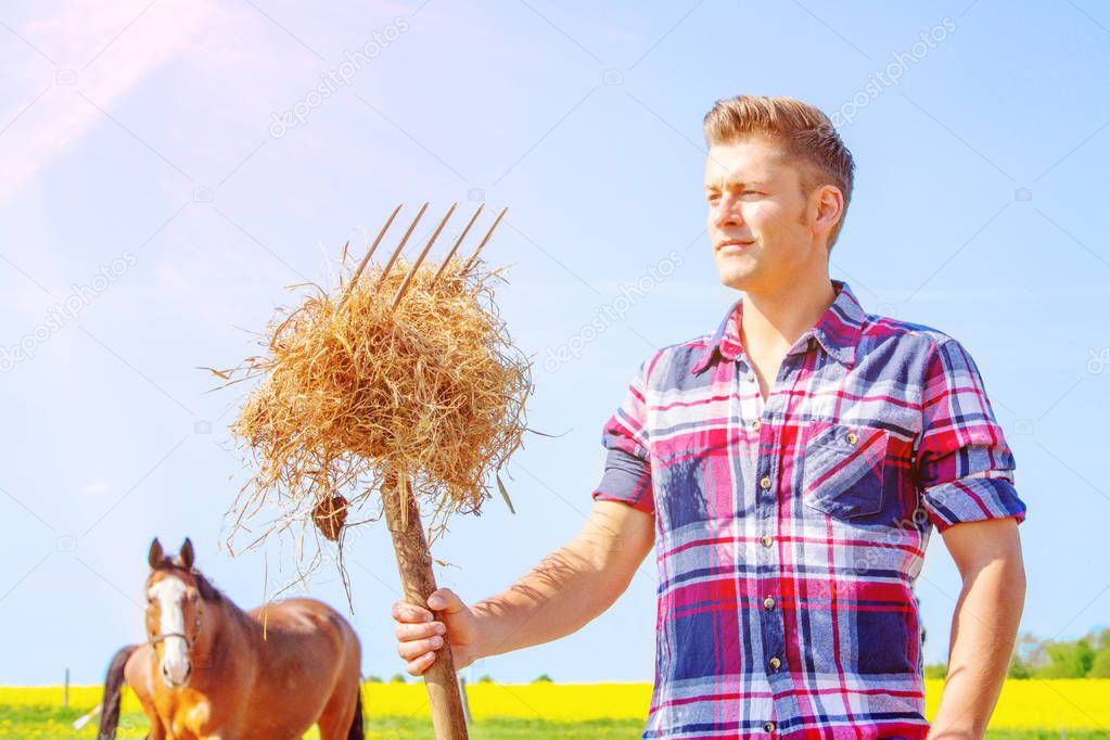 young man with pitchfork and hay and horses in the background