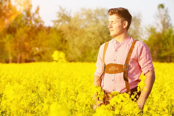 Blond bavarian man standing in a field of yellow flowers — Stock Photo, Image