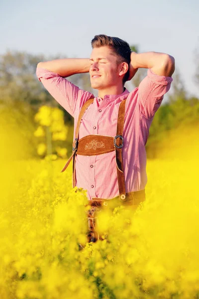 Sarışın Bavyera adam sarı çiçek tarlasında ayakta — Stok fotoğraf