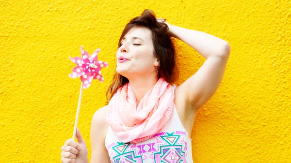 Jonge vrouw stond op gele muur met pinwheel — Stockfoto