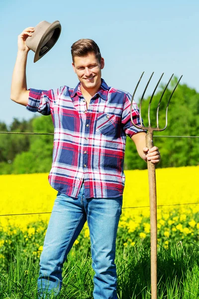 Handsome man with pitchfork standing in front of yellow field — Stock Photo, Image