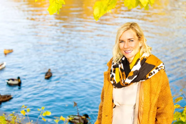 Blond woman standing by lake and enjoying the autumn sun — Stock Photo, Image