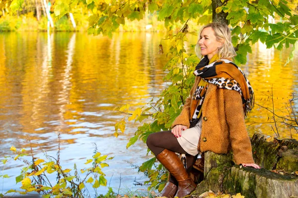 Blonde Frau sitzt am See und genießt die Herbstsonne — Stockfoto