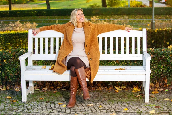 Femme blonde assise sur un banc dans le parc et profitant du soleil d'automne — Photo