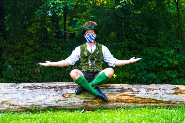 Bayerischer Mann Sitzt Auf Baumstumpf Und Trägt Eine Blauweiße Gesichtsmaske — Stockfoto