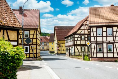 Yarı ahşap evleri ve bulutlu mavi gökyüzü olan küçük bir kötülük manzarası.