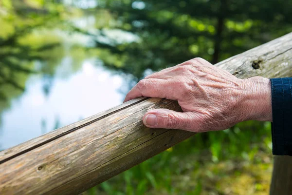 close-up of old womans hand resting at a railing in nature