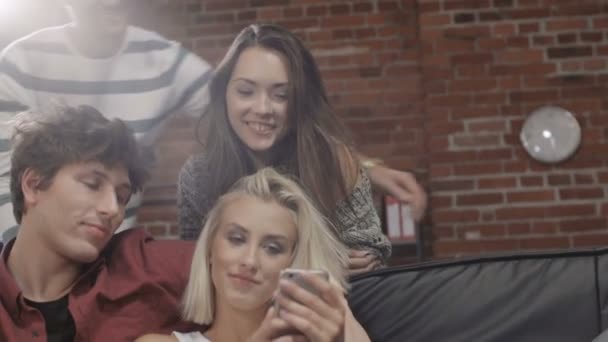 Groep jonge vrienden kijken naar foto's op mobiele telefoon in moderne loft interieur. — Stockvideo