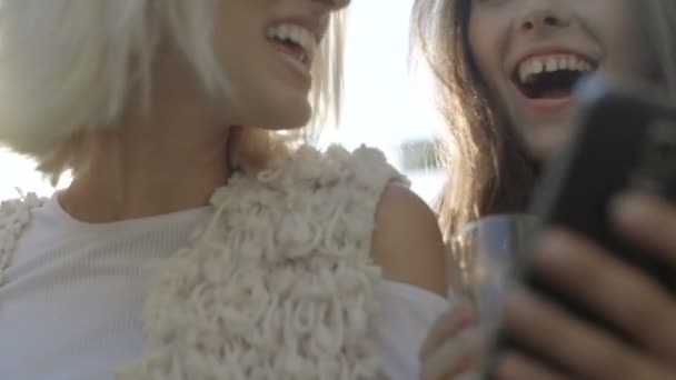 Dos chicas jóvenes felices mirando el teléfono inteligente y divertirse, al aire libre . — Vídeos de Stock