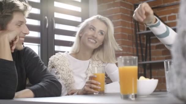 Gruppe junger Freunde unterhält sich an einem Tisch mit gesunden orangefarbenen Getränken in einem Freizeittag im modernen Loft-Interieur. — Stockvideo