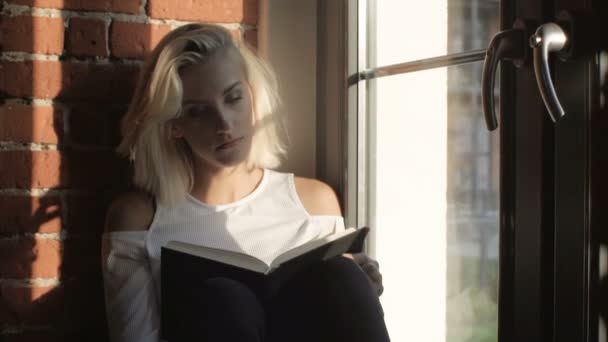 Fiatal nő otthon ül közelében egy ablak, könyv olvasás. — Stock videók