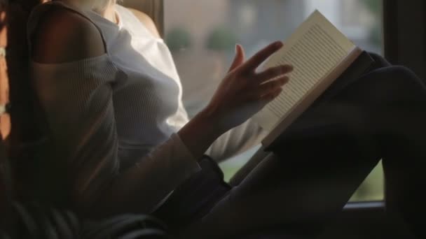 Junge Frau sitzt zu Hause am Fenster und liest Buch. — Stockvideo
