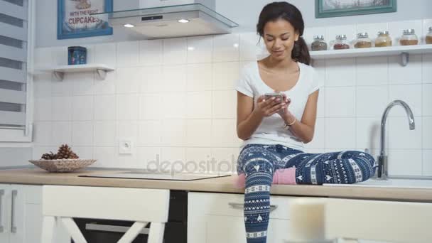 Молодих афро Американку сидять в кухні і писати на мобільний телефон. — стокове відео