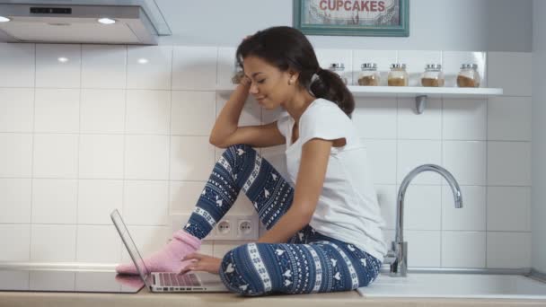 Mujer bastante joven utilizando la computadora en el interior de la cocina moderna . — Vídeo de stock