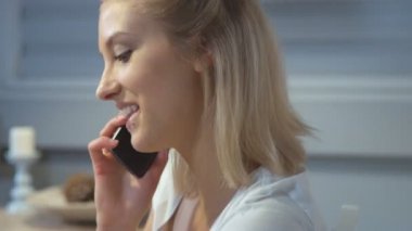 Genç bir beyaz kadın bir mutfakta otururken cep telefonu üzerinde konuşurken yakın çekim.