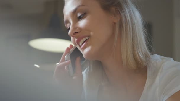 Close up de uma jovem caucasiana falando no telefone celular enquanto está sentado em uma cozinha . — Vídeo de Stock