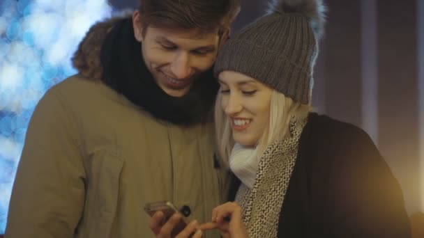 Молода пара дивиться фотографії на смартфон вночі на міській вулиці . — стокове відео