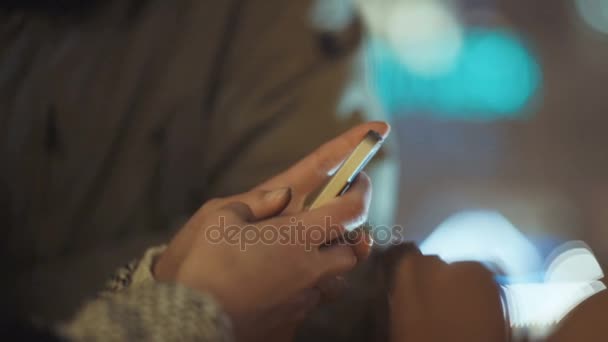 Pareja joven viendo fotos en el teléfono inteligente por la noche en una calle de la ciudad . — Vídeos de Stock