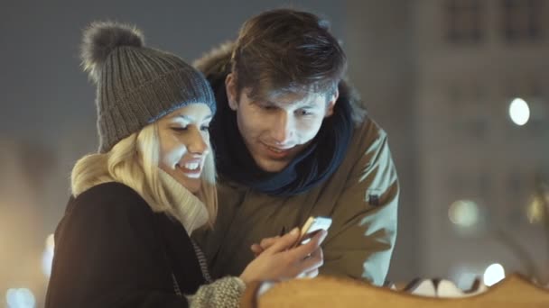 Молода пара дивиться фотографії на смартфон вночі на міській вулиці . — стокове відео