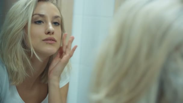 Νεαρή γυναίκα ελέγχοντας το πρόσωπό της στον καθρέφτη του μπάνιου στο σπίτι. — Αρχείο Βίντεο