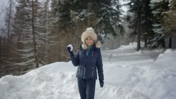 Hermosa chica en ropa de invierno lanzando una bola de nieve en la cámara . — Vídeos de Stock