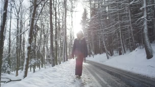 Mujer vestida con ropa de abrigo caminando en un frío bosque de nieve de invierno . — Vídeos de Stock