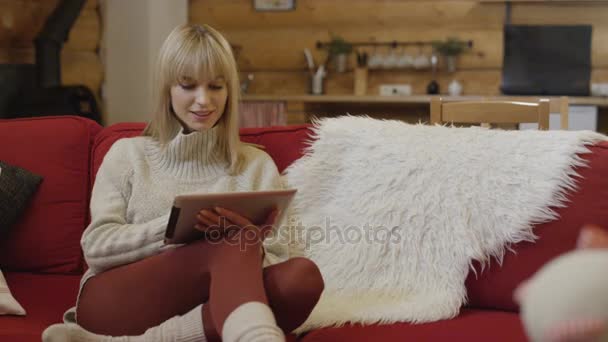 美丽的女孩，穿了件毛衣在冬季使用一台平板电脑在家里. — 图库视频影像