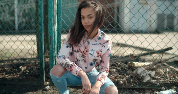 Portrait d'une jeune femme afro-américaine portant une veste de bombardier posant sur une clôture en métal, à l'extérieur . — Photo