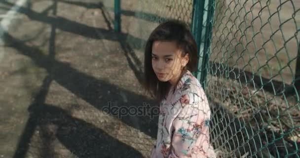 Metal çitin üzerinden poz bombardıman ceket giyen genç güzel kadın. — Stok video