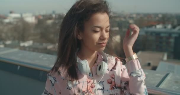 Young woman with headphones enjoying time on a rooftop. — Stock Video