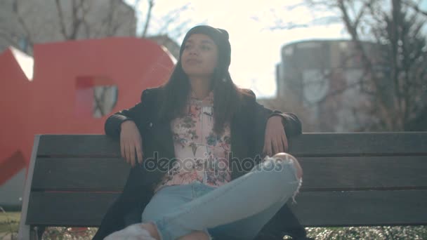 Bir bankta oturan genç güzel Afrikalı-Amerikalı kadın. — Stok video