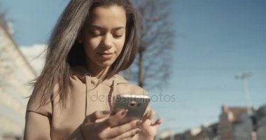 Güzel genç kadın telefonla güneşli gün boyunca yazarak.