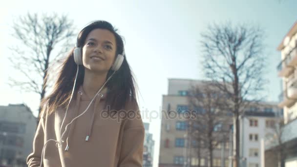 Ung kvinna med hörlurar njuta av tid i en stad. — Stockvideo