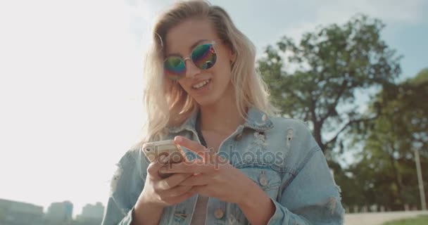 Jonge blonde vrouw met behulp van telefoon in een stad. — Stockvideo