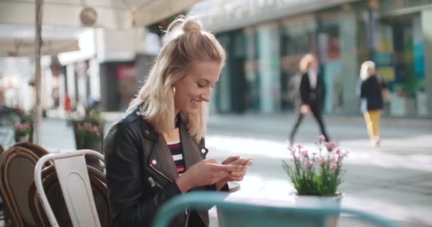 Joven mujer caucásica escribiendo por teléfono en un café de la ciudad . — Vídeos de Stock