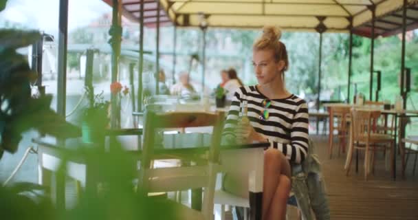 Hezká mladá kavkazské dívka sedí u venkovní kavárna a čeká na někoho. — Stock video