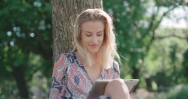 Genç kadın parkta oturan ve dijital tablet kullanma.