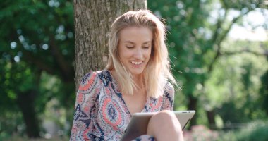 Genç kadın parkta oturan ve dijital tablet kullanma. 